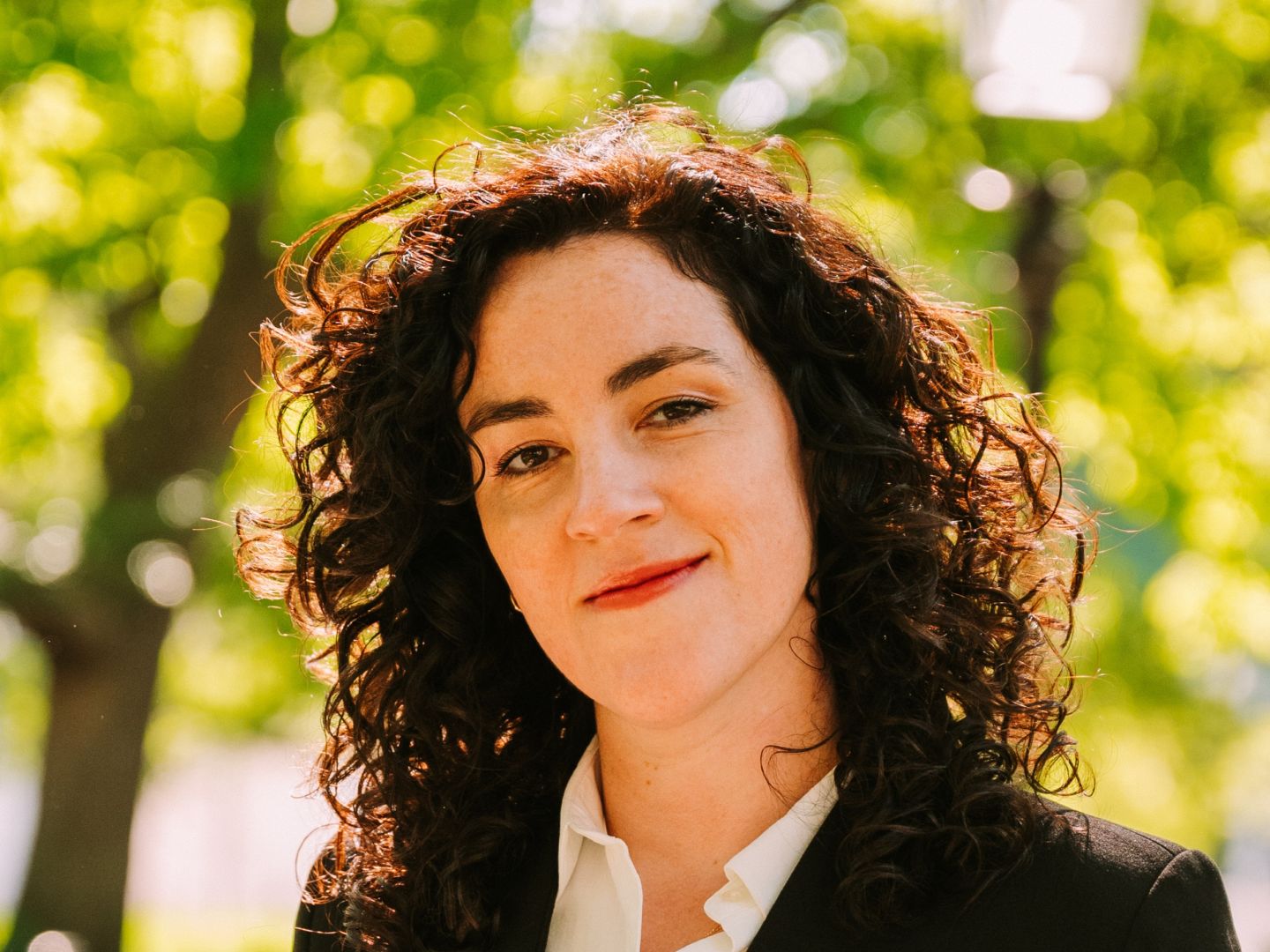 Portraitfoto von Julia Prechsl im Anzug vor grünen Bäumen.