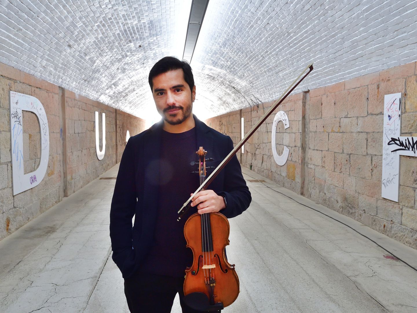 Gustavo Strauß mit Violine in der Hand steht in einem Tunnel.