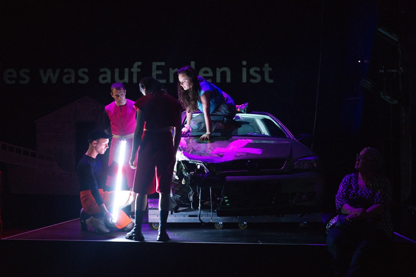 Das Bild zeigt mehrere Personen, die um ein Auto stehen. Ein Mann hält einen Leuchtstab in der Hand und inspiziert das Auto.