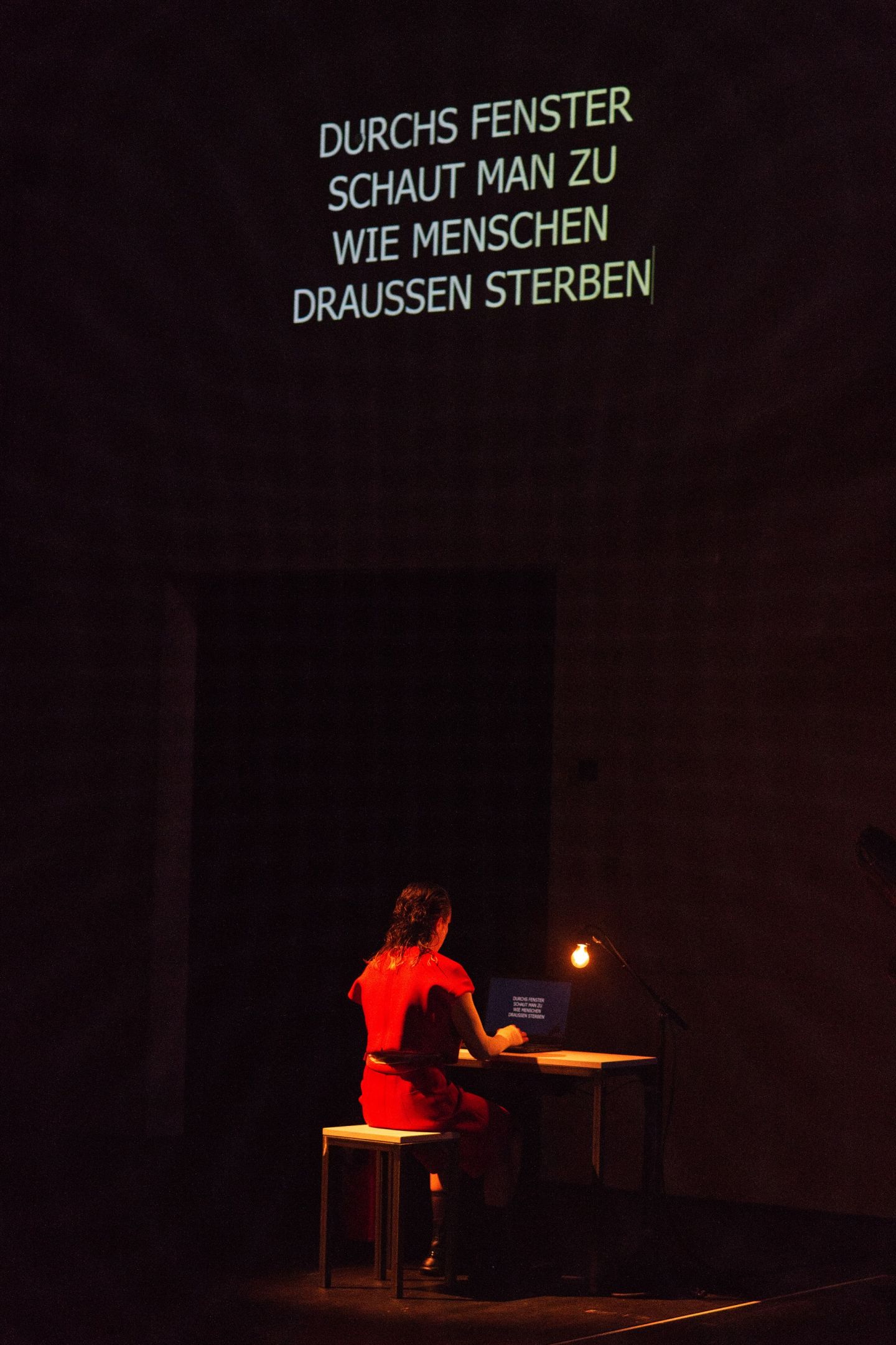 Das Bild zeigt eine Frau, die an einem Tisch sitzt und auf einer Tastatur tippt. Ihr Text wird an die Wand projiziert.