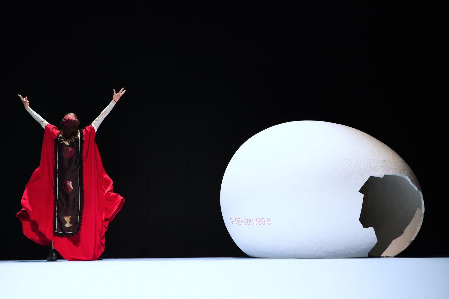 Eine Person in rot streckt die Arme über den Kopf und steht neben einer kaputten Eierschale.