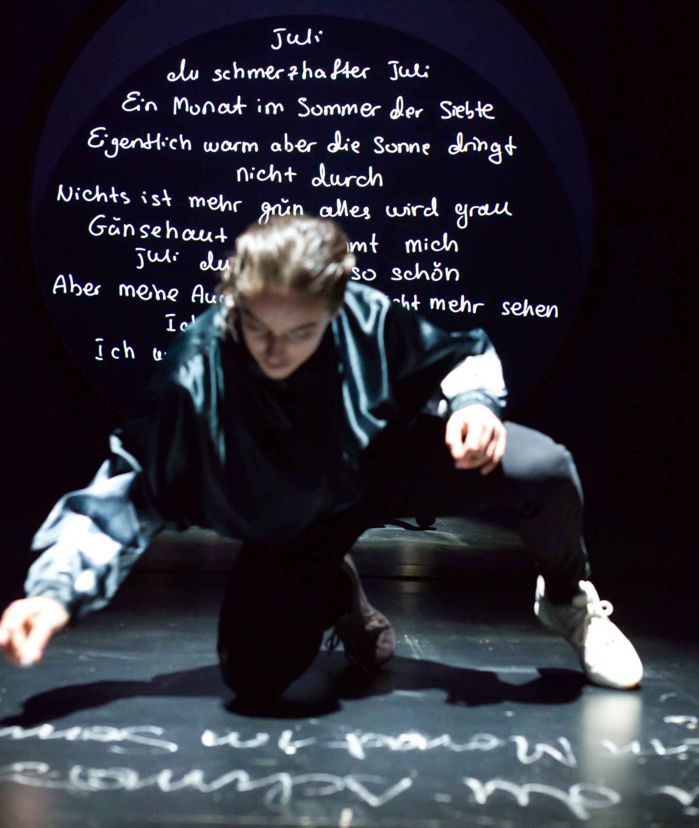 Ruth Bohsung schreibt mit Kreide das Gedicht "Juli" auf den Boden. Im Hintergrund ist es auf eine Wand projiziert.