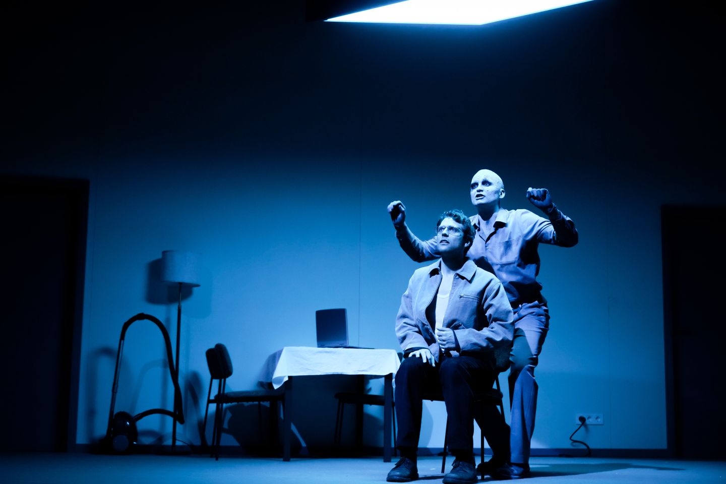 Anton Nürnberg als Krähe steht gestikulierend hinter Silas Breiding als Vater, der auf einem Stuhl sitzt.