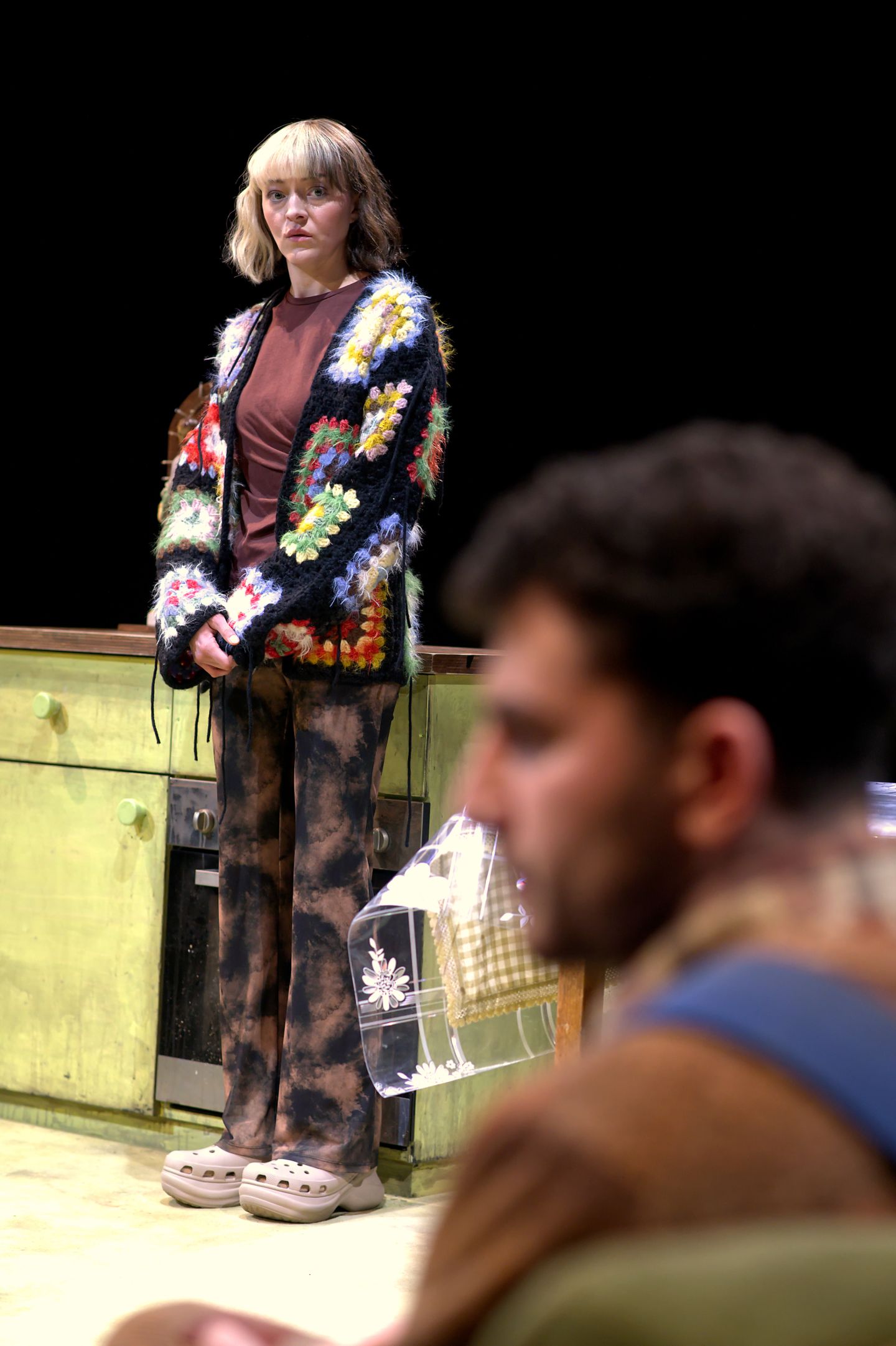 Eine Schauspielerin steht, ein Schauspieler sitzt auf der Couch