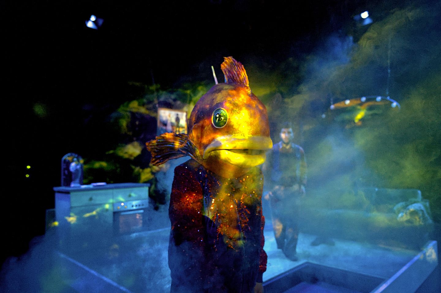 Ein Schauspieler mit einer Fischmaske auf dem Kopf steht im Raum.
