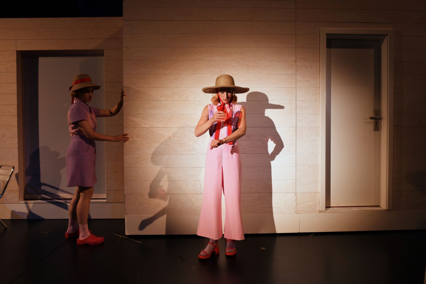 Zwei Schauspielerinnen in Sommerhüten stehen vor einer Hausfassade.