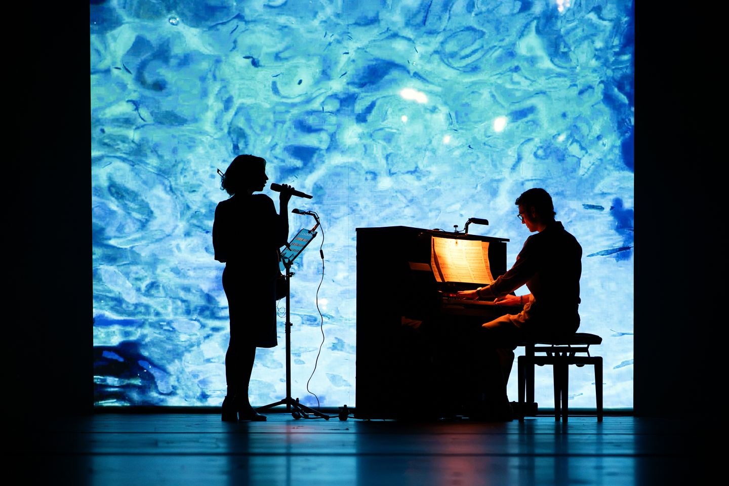 Zwei Silhouetten vor einer Videoprojektion von Wasser.
