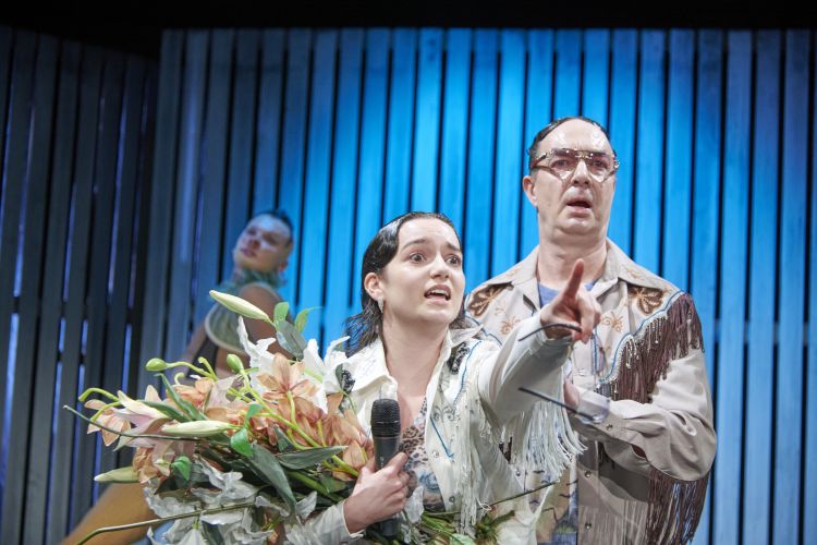 Eine Spielerin mit einem Blumenstrauß zeigt einem anderen Spieler etwas.