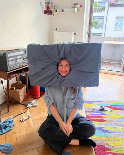 Rebecca Fischer trägt eine Kissenartige Attrappe auf ihrem Kopf, nur ihr Gesicht ist noch frei.