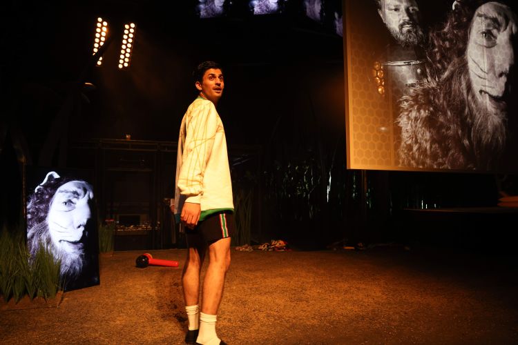 Ein Schauspieler im Fußballtrikot blickt über die Schulter. Neben im Ein Bildschirm mit einem als Löwen geschminkten Schauspieler.