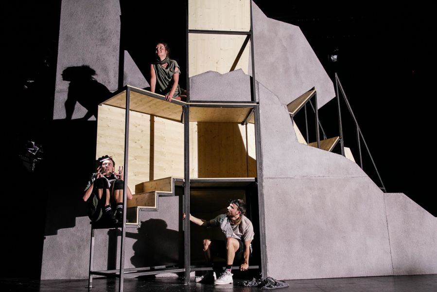Drei Männer sitzen in einem felsenartigen Bühnenbild.