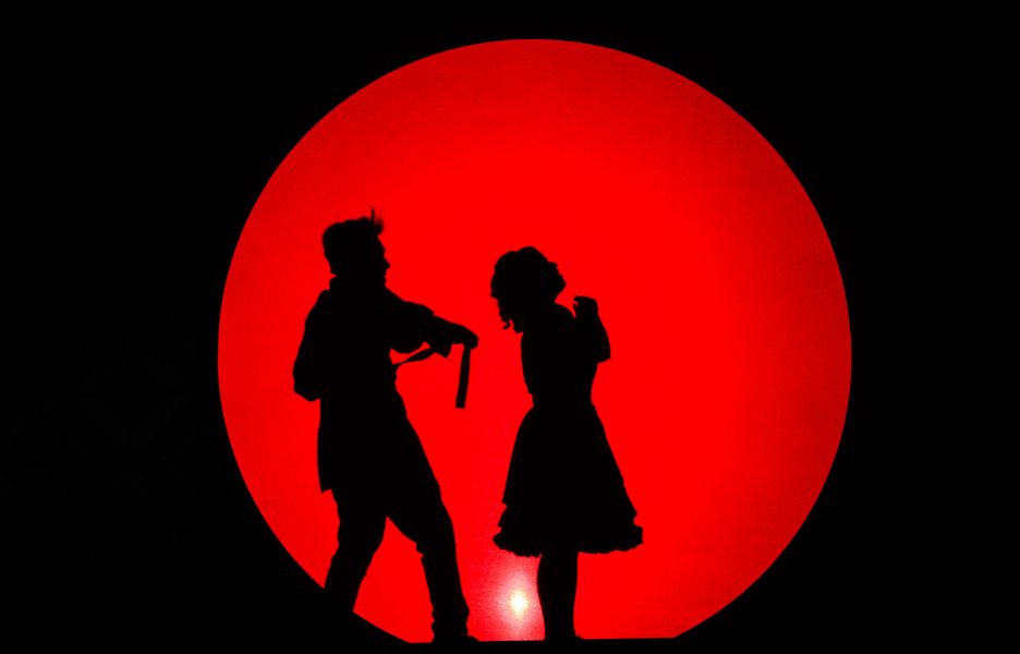 Das Foto zeigt zwei Silhouetten, die vor einem großen roten Kreis stehen.