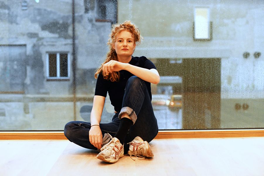 Das Foto zeigt Liv Stapelfeldt im Volkstheater auf dem Boden sitzend vor großem Fenster
