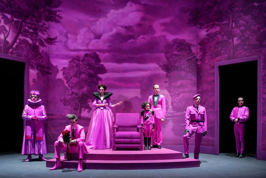 Das Foto zeigt das Ensemble, das pink gekleidet um einen Sessel platziert steht.