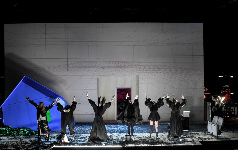 Das Foto zeigt das Ensemble in schwarzer Kleidung, das aufgereiht am Bühnenrand steht und die Hände in die Luft streckt.