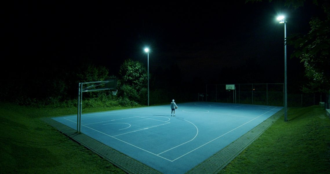 Das Foto zeigt einen Mann auf einem Basketballplatz im Dunkeln