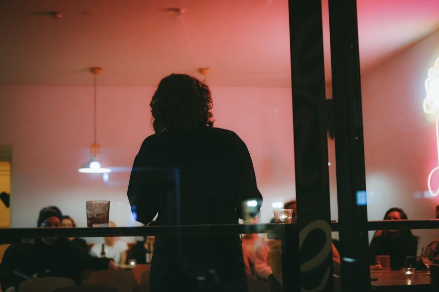 Ein Bild von einer Person von hinten mit einem Cafe/Bar im Hintergrund.