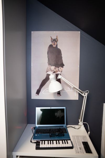 Ein Foto von einem Schreibtisch mit Laptop und Lampe, an der Wand dahinter hängt ein Poster.