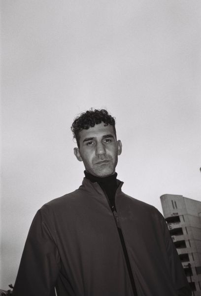 Ein Portrait von Necati Öziri in schwarz weiß. Hinter ihm ist ein Hochhaus zu sehen.