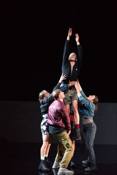 Ruth Bohsung, Max Poerting Jonathan Müller und Nina Steils in ihren Rollen heben Julian Gutmann in seiner Rolle in die Höhe. Er reckt sich nach oben.