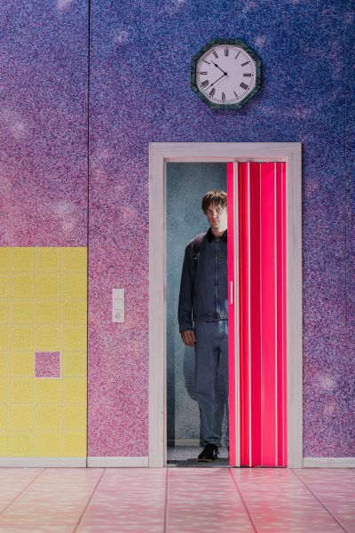Ein Schauspieler in schwarz gekleidet im bunten Bühnenbild